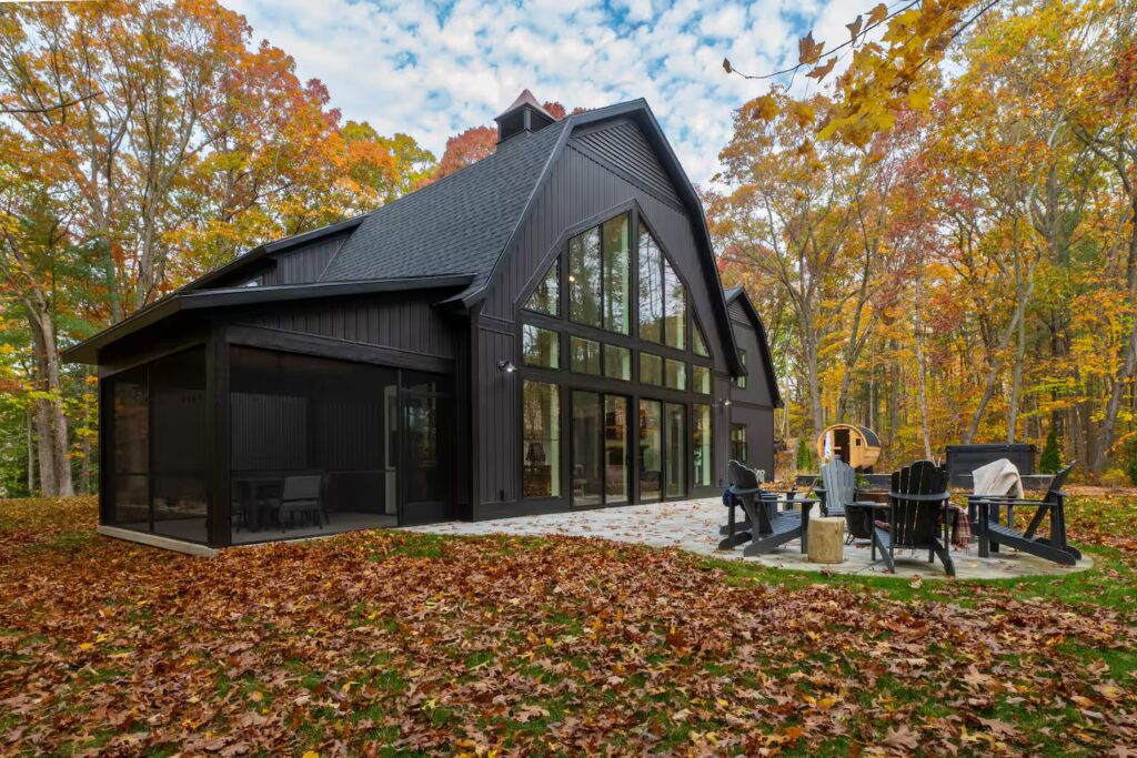 Glass rear facade of the barn house among autumn leaves.